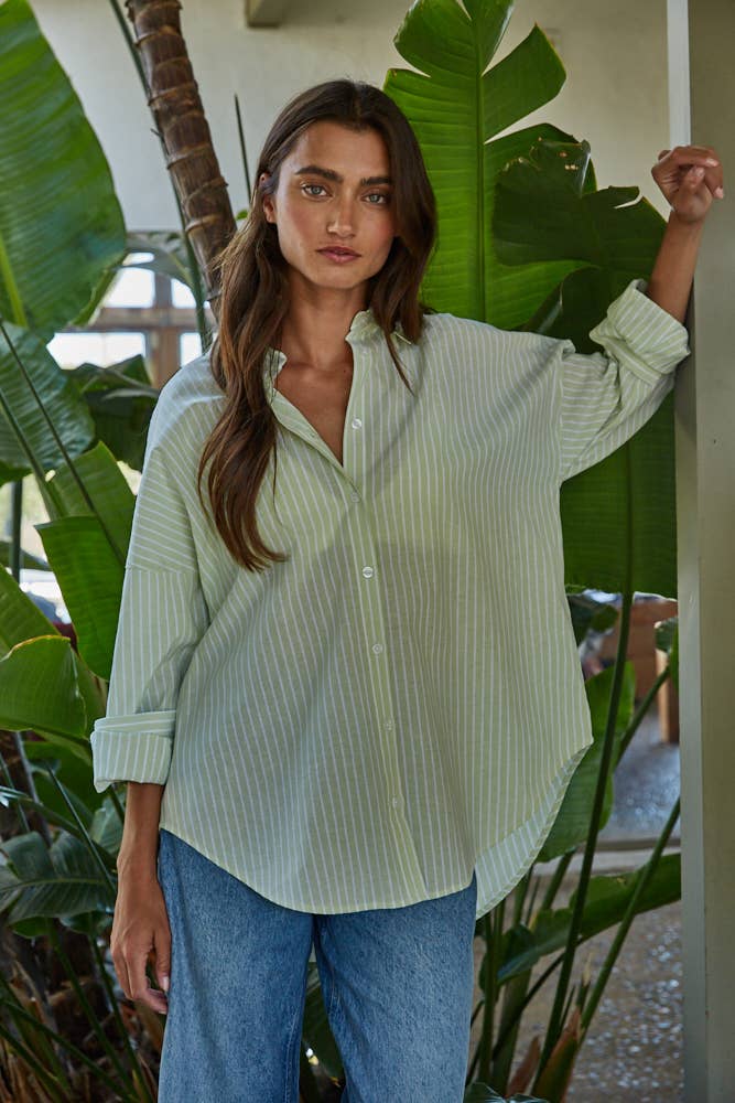 Woman wearing a light green button down shirt and blue jeans standing among plants.