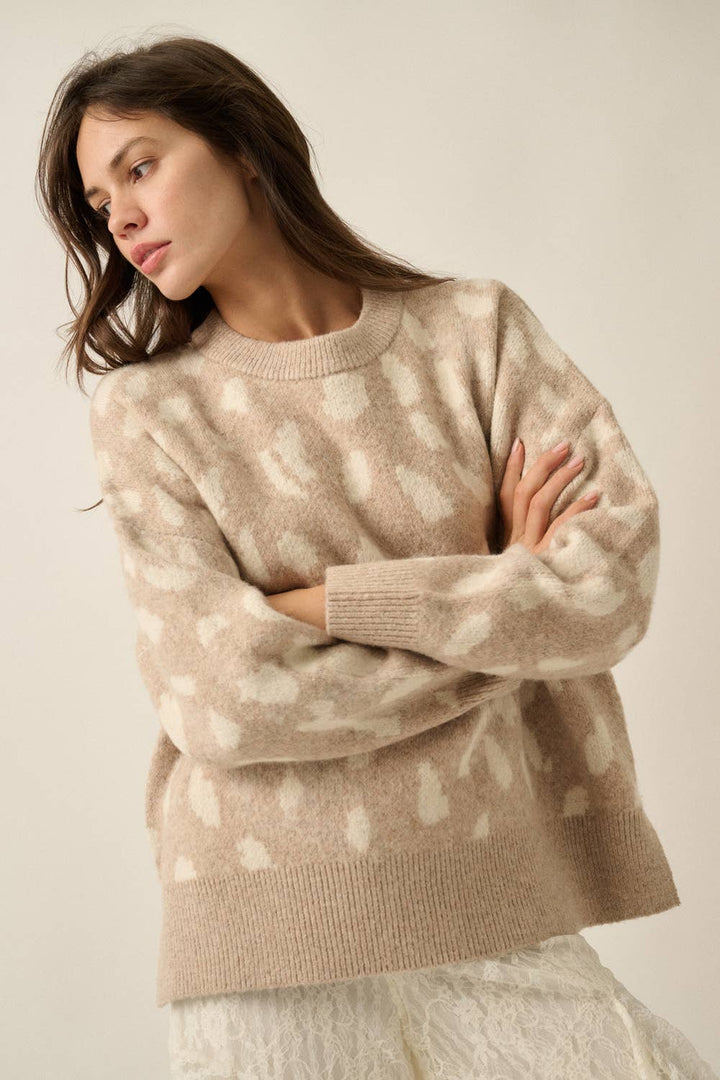 A woman wearing a beige crewneck knit sweater with a white bambi print pattern, posed with her arms crossed against a plain light beige background.
