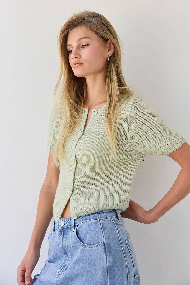 Woman wearing a light green knitted cardigan and blue jeans against a white background
