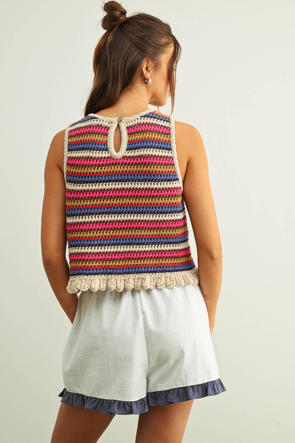 Woman wearing a colorful striped sleeveless crochet knit top and white shorts on a plain background