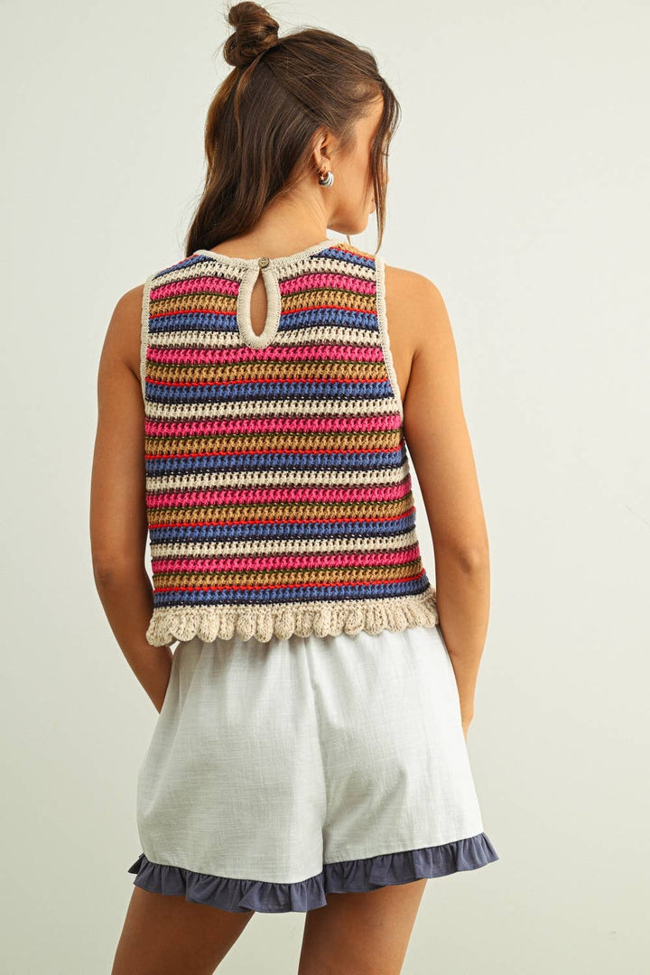Woman wearing a colorful striped sleeveless crochet knit top and white shorts on a plain background