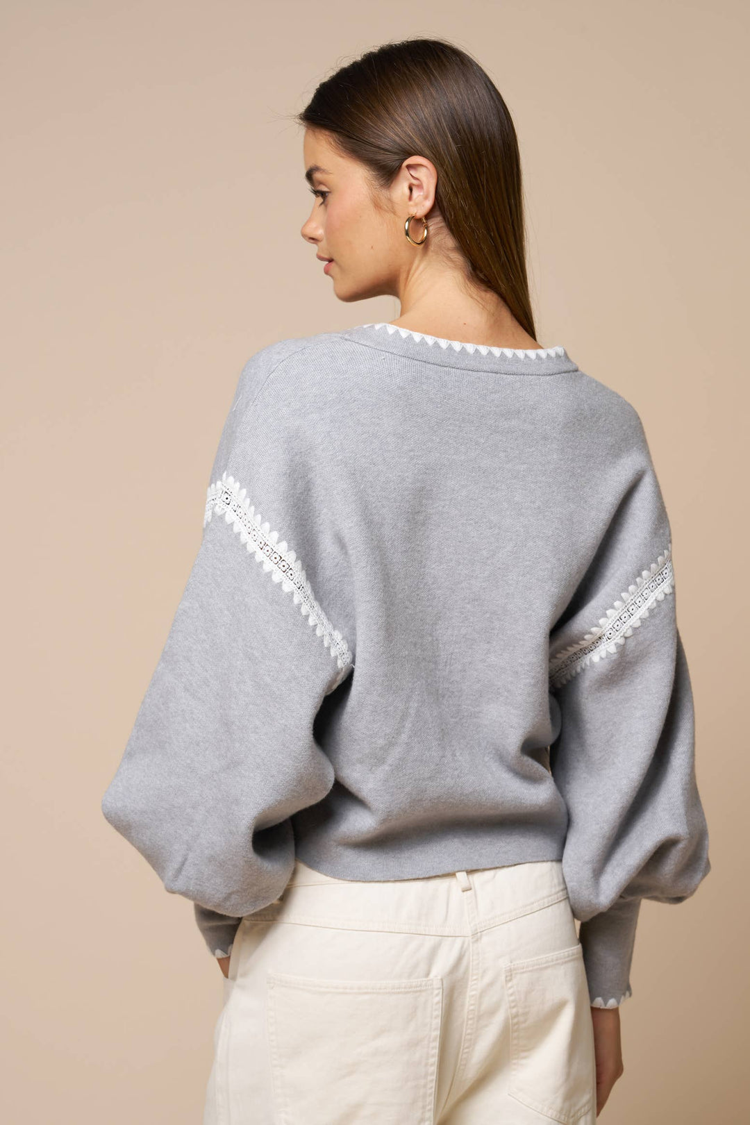 Woman wearing a gray sweater with white trim on a beige background