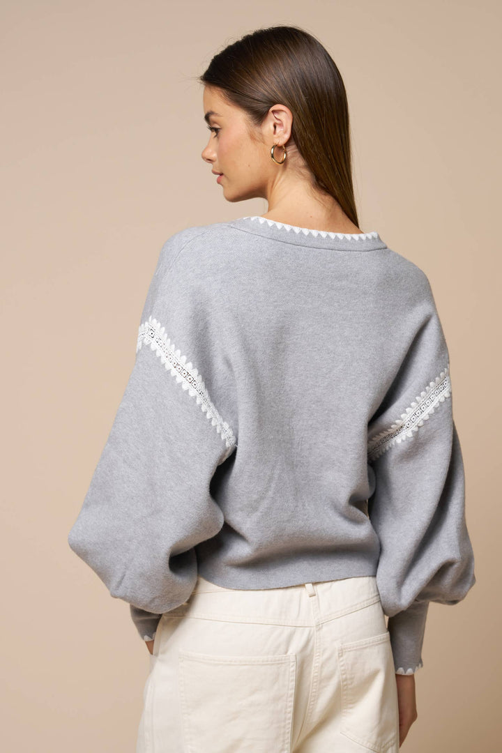 Woman wearing a gray sweater with white trim on a beige background