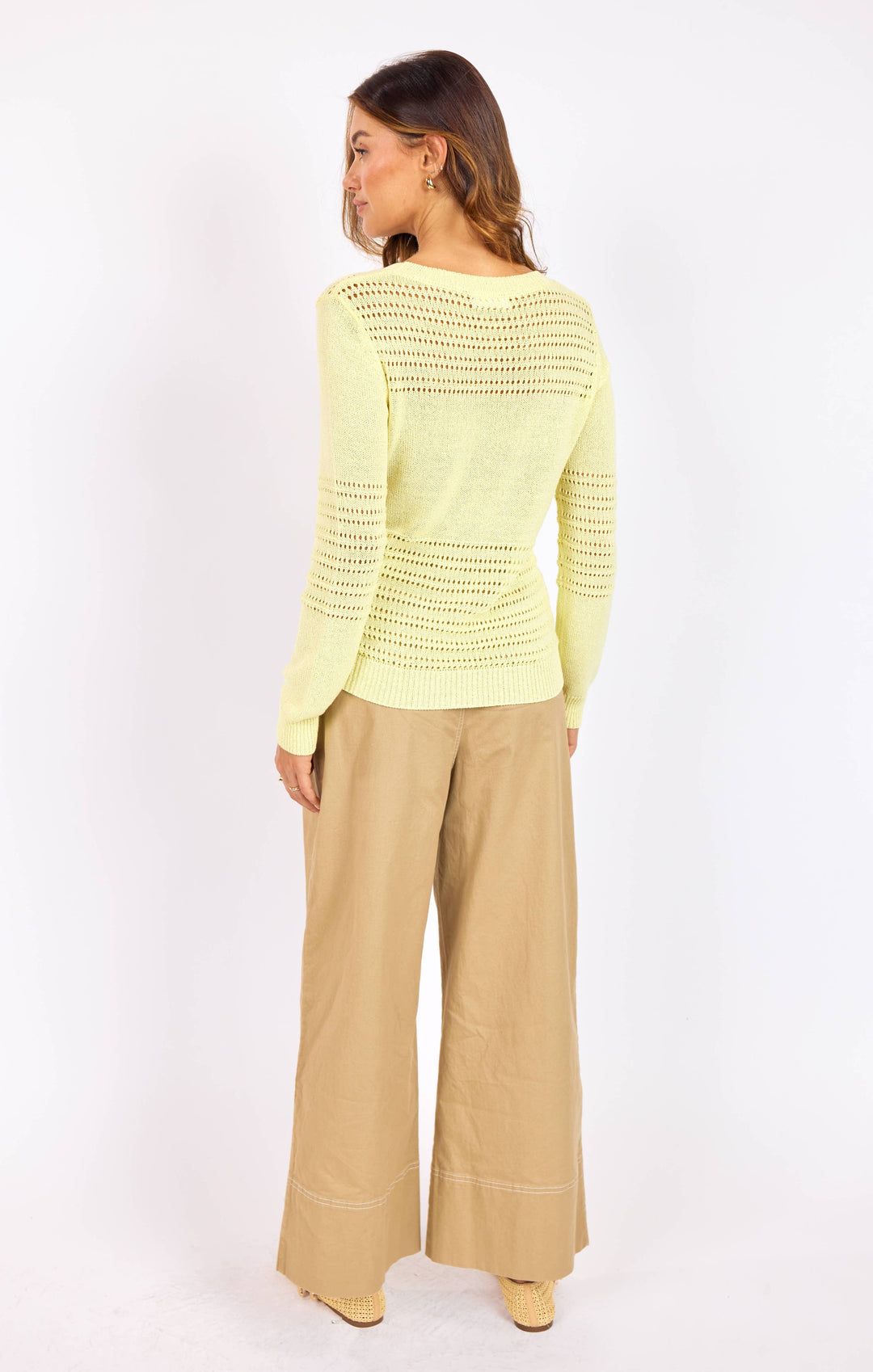 Woman wearing a light yellow crochet sweater and beige pants on a white background