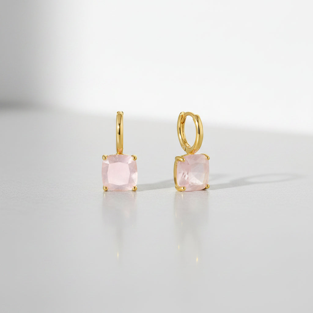 Gold earrings with pink gemstones on a white background