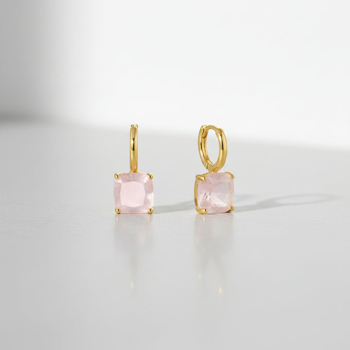 Gold earrings with pink gemstones on a white background