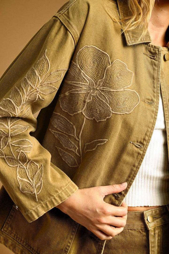 Close-up of a woman wearing an khaki denim embroidered jacket with floral embroidery.