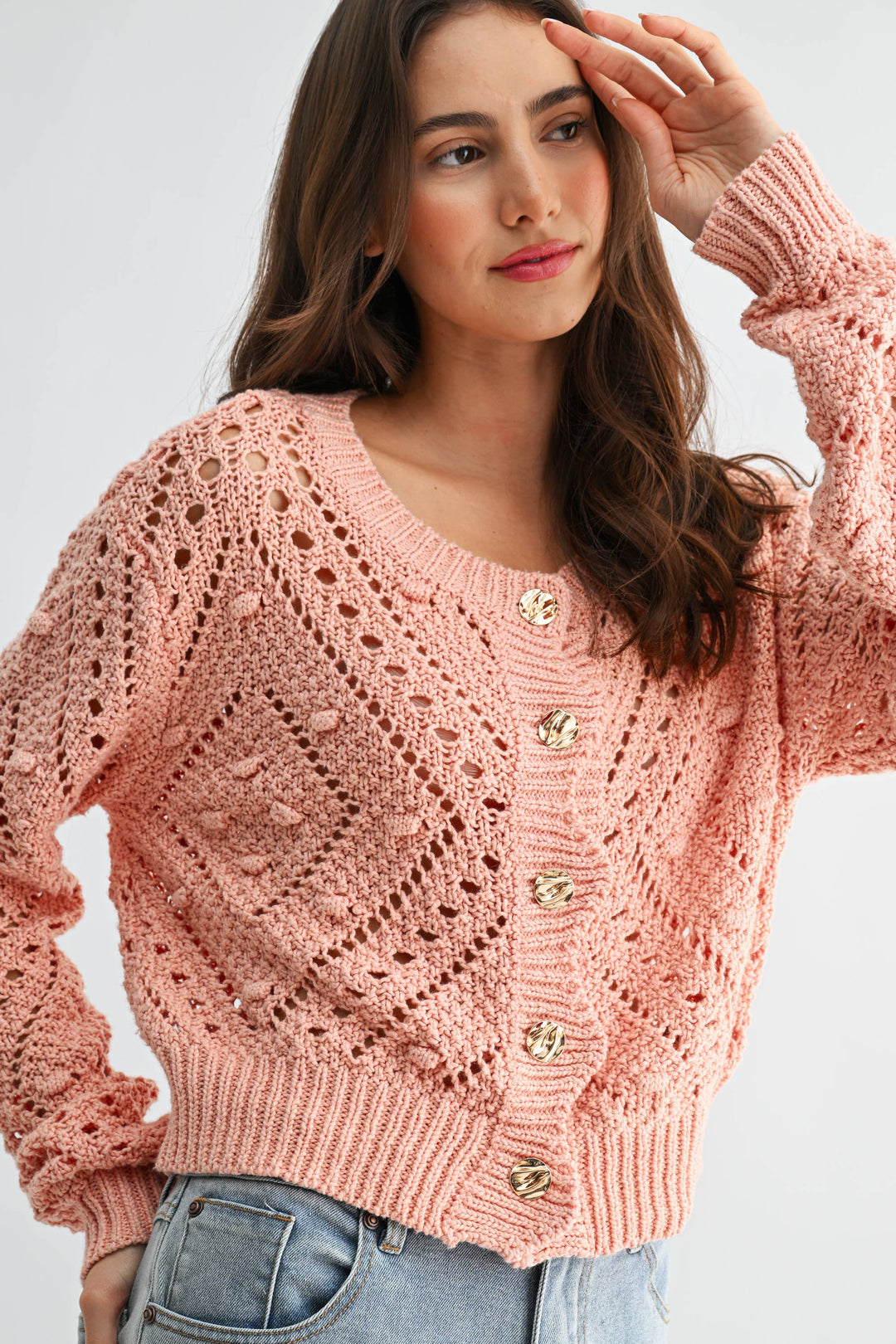 Woman wearing a pink knitted cardigan with gold buttons on a light gray background