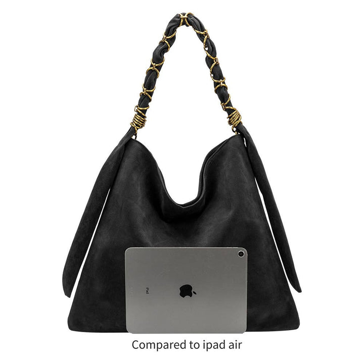 A black slouchy shoulder bag with braided black and gold handles, shown against a white background with a gray iPad Air placed inside the bag for scale and the text &