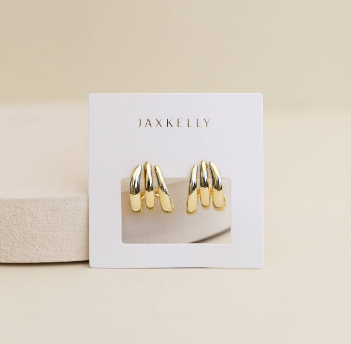 Gold earrings on a Jax Kelly branded card against a beige background