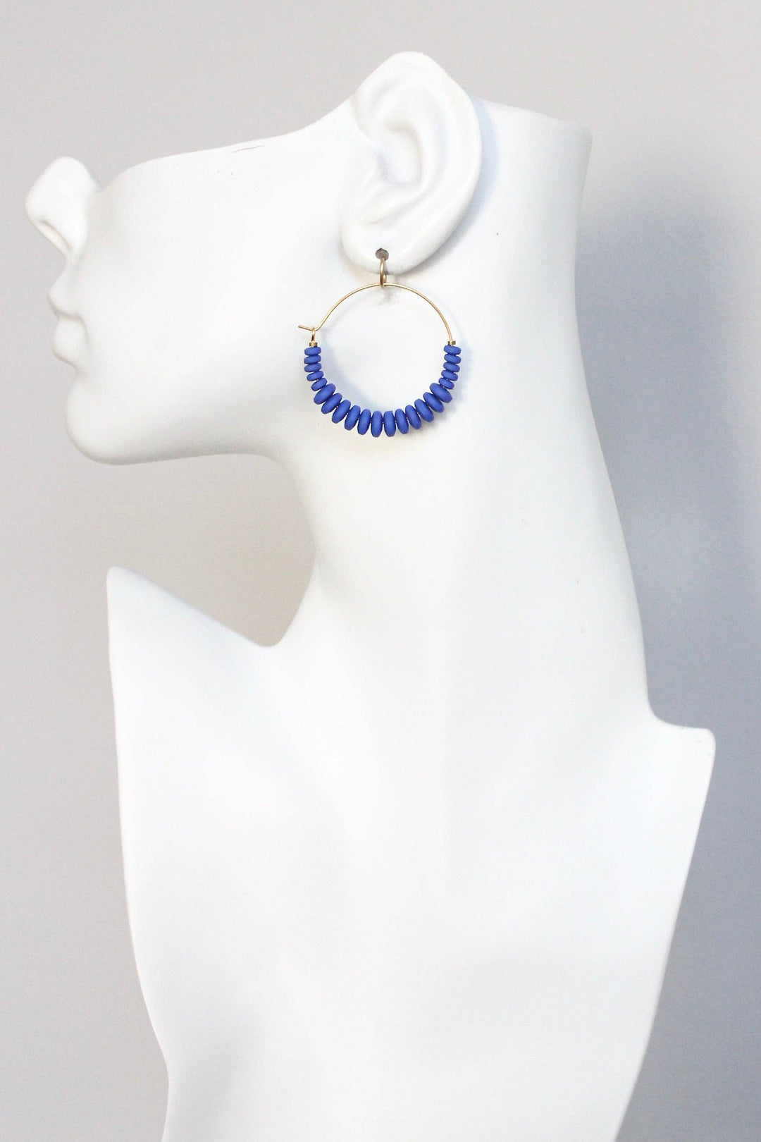 Blue beaded hoop earrings on a mannequin ear against a gray background