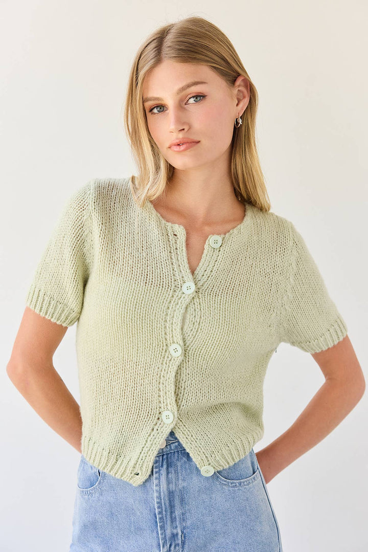Woman wearing a light green knitted short sleeve cardigan and blue jeans on a white background