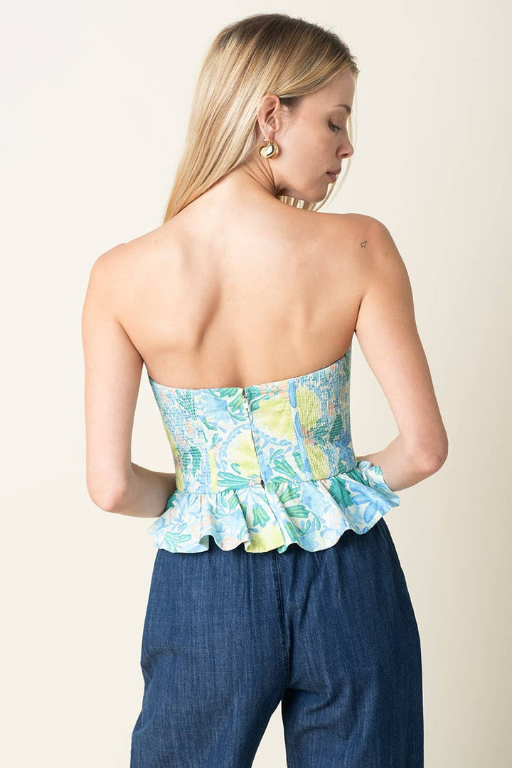 Woman wearing a strapless floral top and blue pants against a plain background