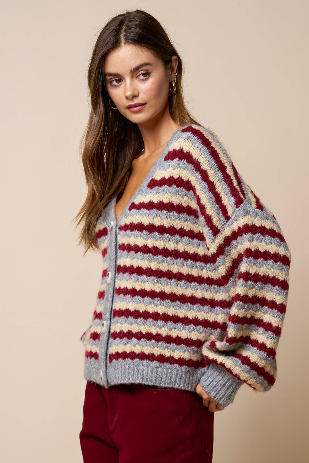 Woman wearing a mulberry and gray striped oversized cardigan with a beige background