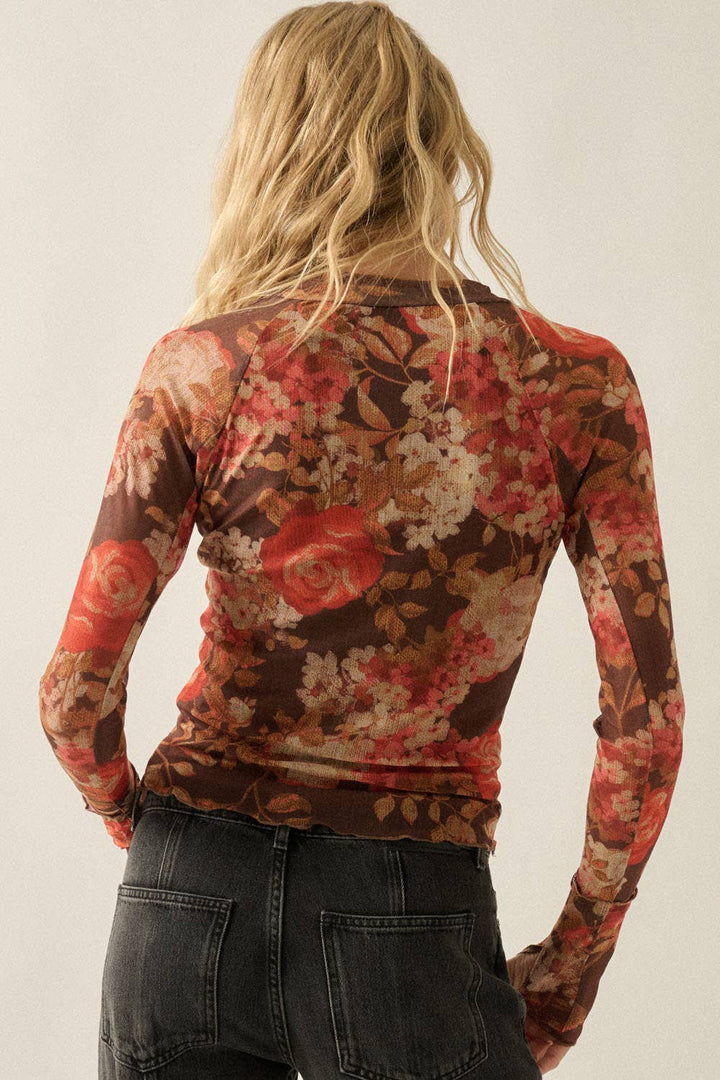 A woman viewed from behind wearing a fitted long-sleeve top with a dense floral print in brown, rust red, beige, and cream tones, paired with dark jeans against a plain light background.