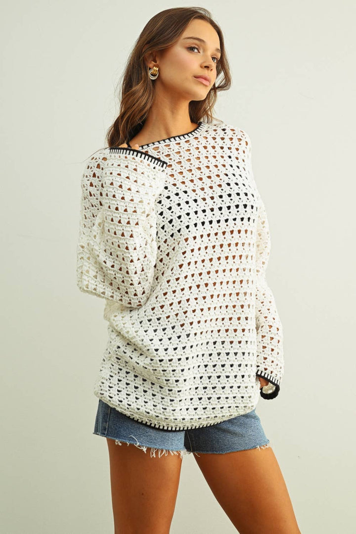 Woman wearing a white crochet sweater and denim shorts on a plain background