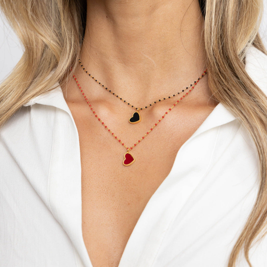 Two necklaces with heart pendants on a person wearing a white shirt.