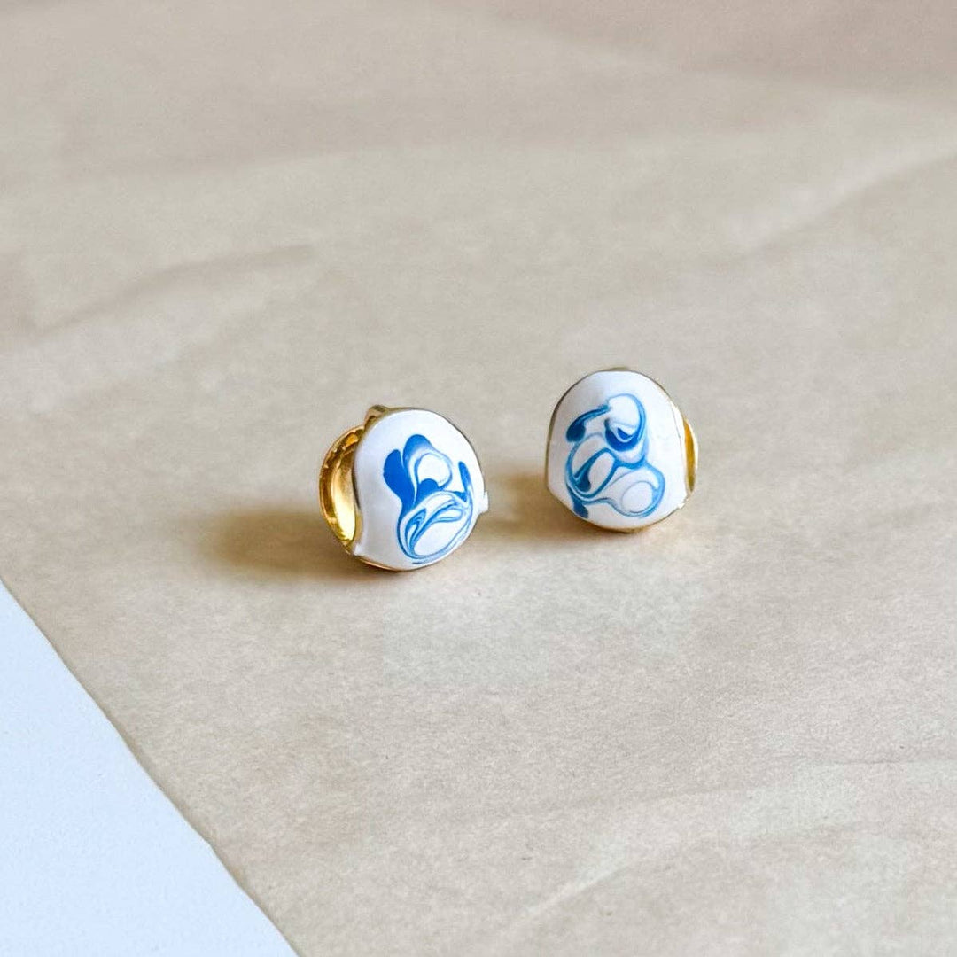 Pair of round earrings with blue designs on a beige surface
