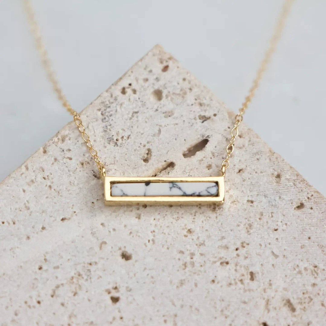 Gold necklace with a marbled dainty bar pendant on a textured stone surface