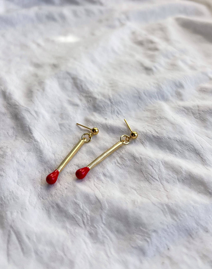 Gold earrings with red accents on a white marble surface
