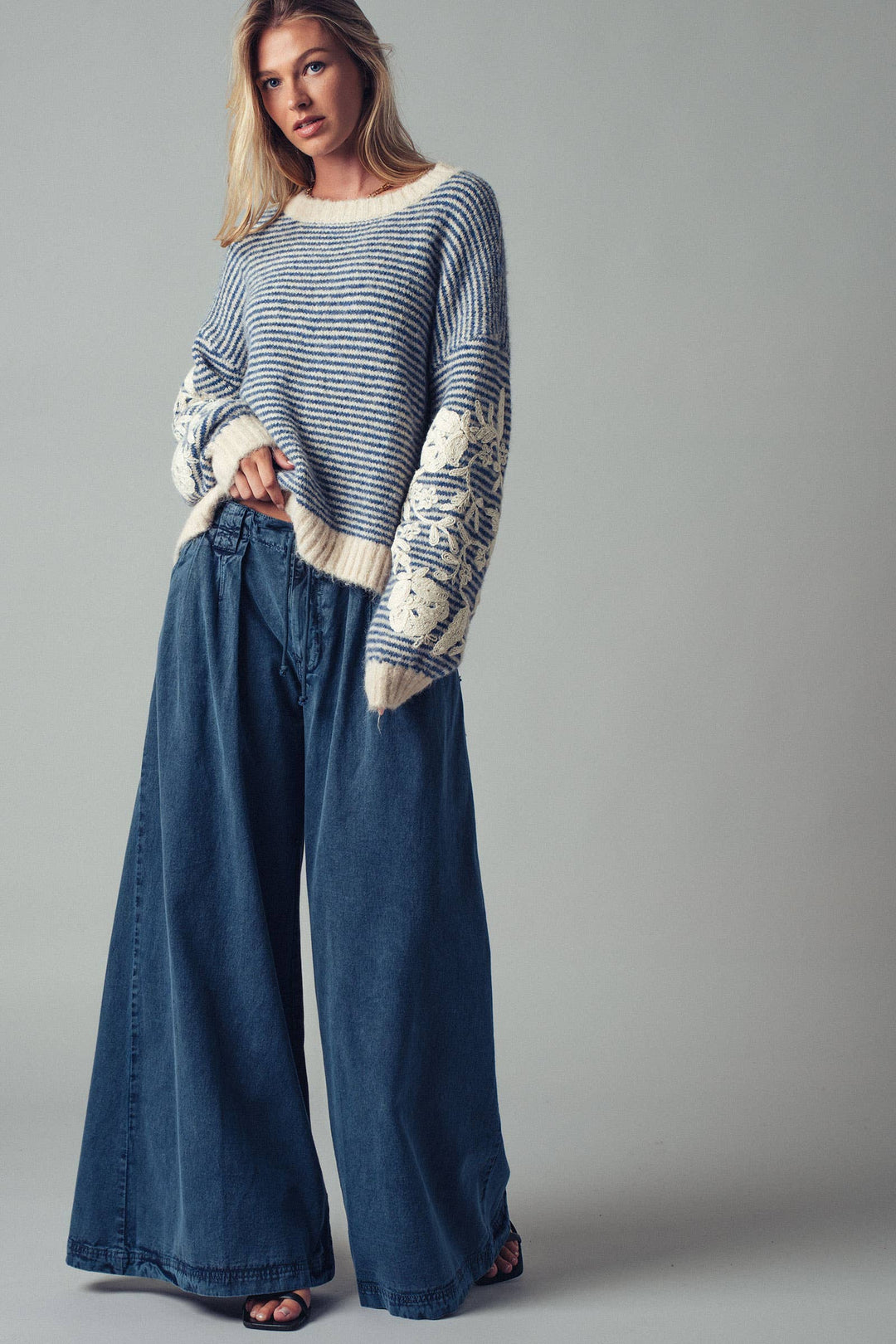 Woman wearing a blue striped sweater and wide-leg jeans against a gray background