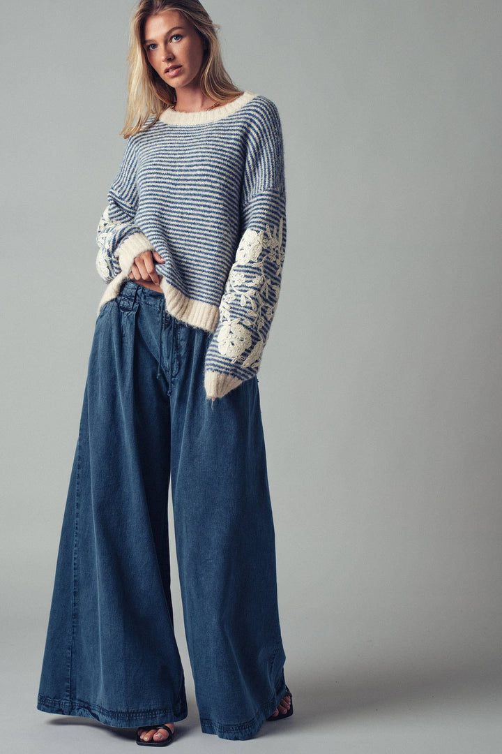 Woman wearing a blue striped sweater and wide-leg jeans against a gray background