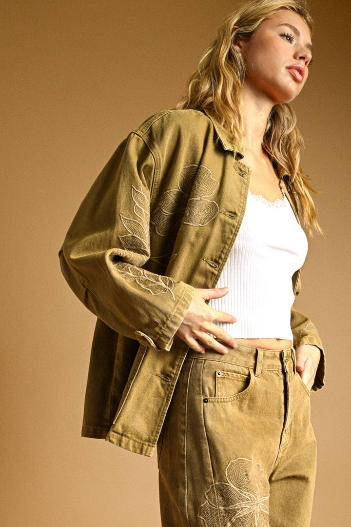 Woman wearing a beige jacket and matching pants set with a white top against a brown background