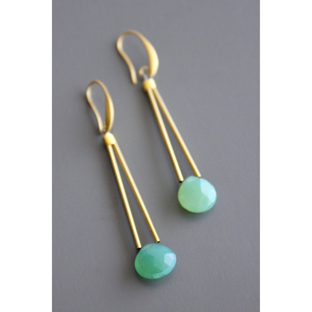 Gold dangle earrings with blue green beads on a gray background