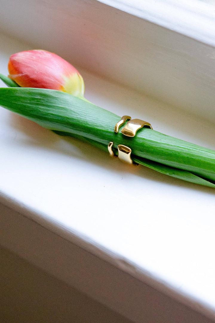 Gold double stacking ring on a green stem with a pink tulip in the background