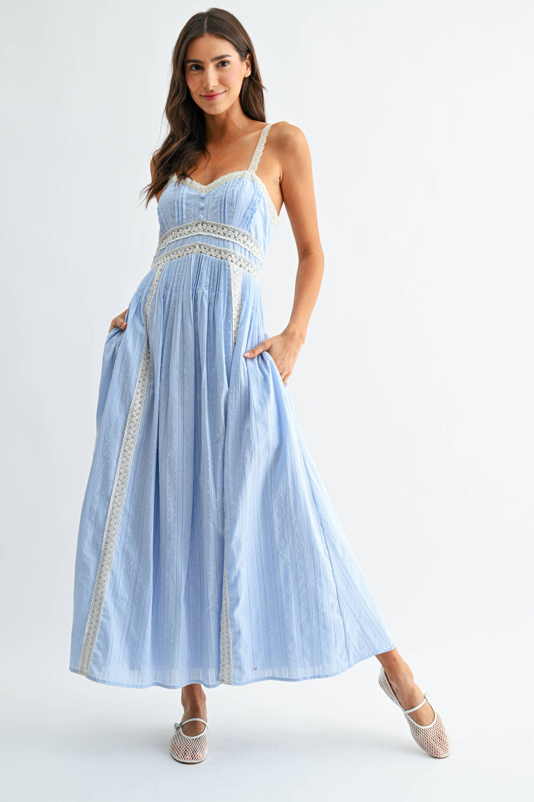 Woman wearing a light blue midi summer dress with white lace trim on a white background