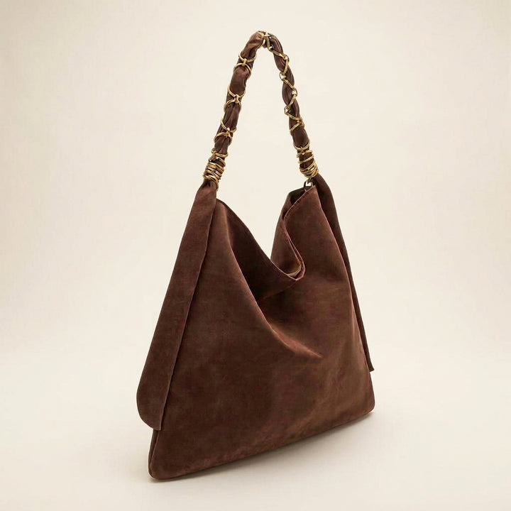A brown vegan suede slouchy shoulder bag with a braided leather handle accented by gold-tone metal rings, shown on a plain white background.