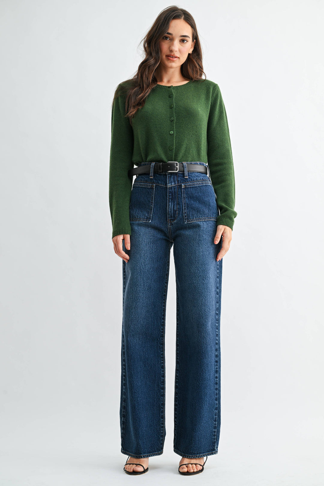 Woman wearing a green sweater and blue jeans on a white background