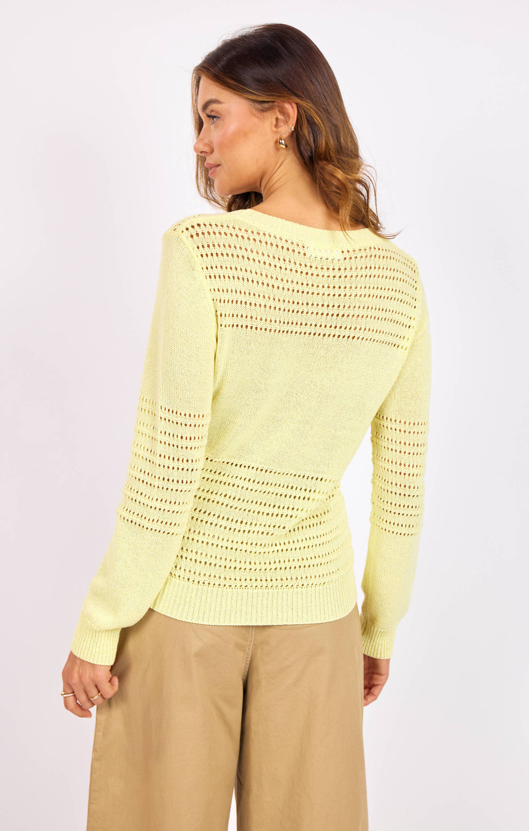 Woman wearing a light yellow crochet sweater on a white background