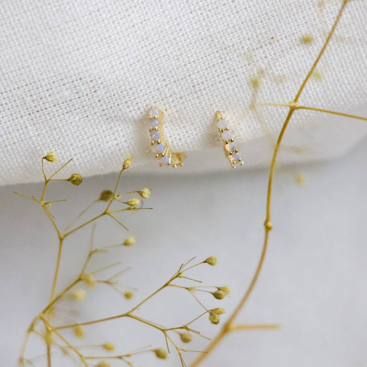 Gold earrings with small opalite stones on a white fabric background