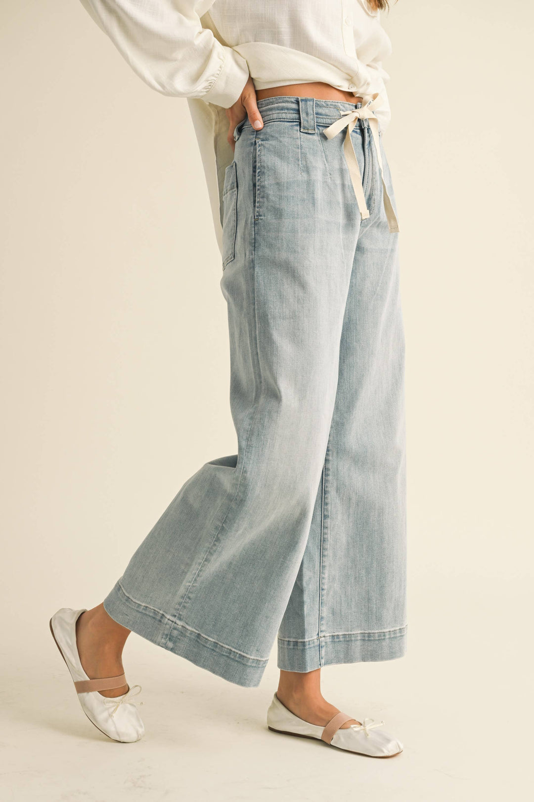 Light blue denim wide leg cropped jeans with drawstring worn by a woman a beige background