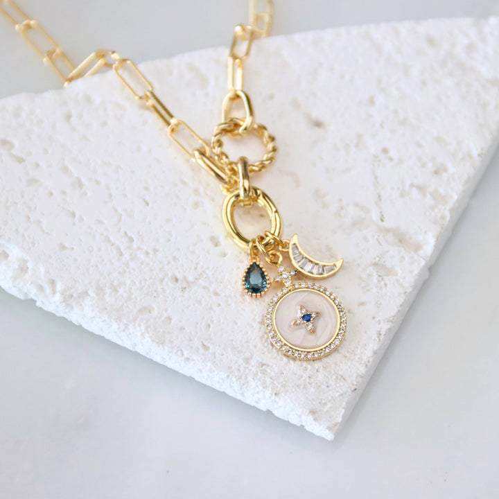 Gold necklace with gemstone and CZ charms on a textured white surface