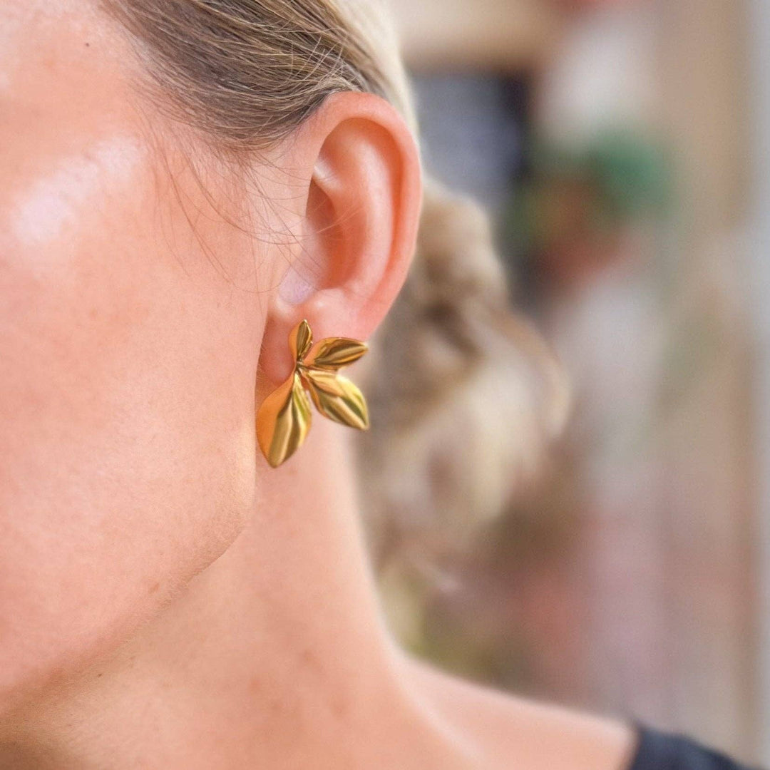 Gold leaf shaped statement earring worn by a person with a blurred background