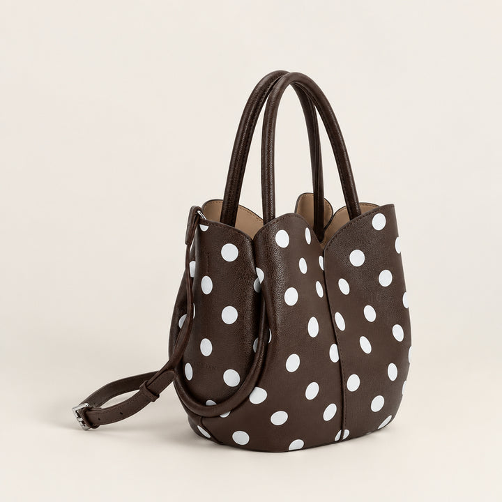 A dark brown pebbled leather handbag with a white polka dot pattern, featuring dual top handles and a detachable shoulder strap, shown against a plain white background.