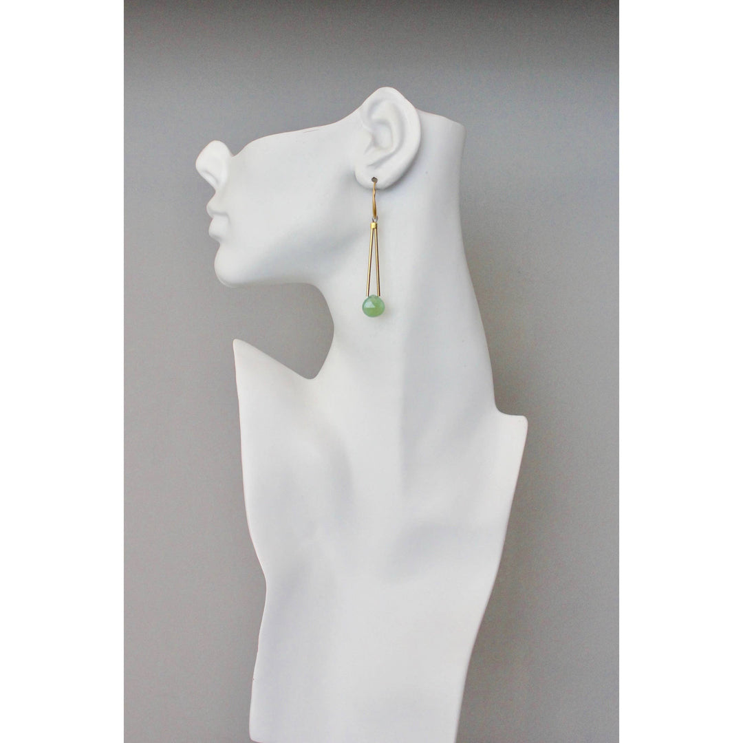 Gold dangle earring with blue-green bead on a white mannequin ear with a plain background