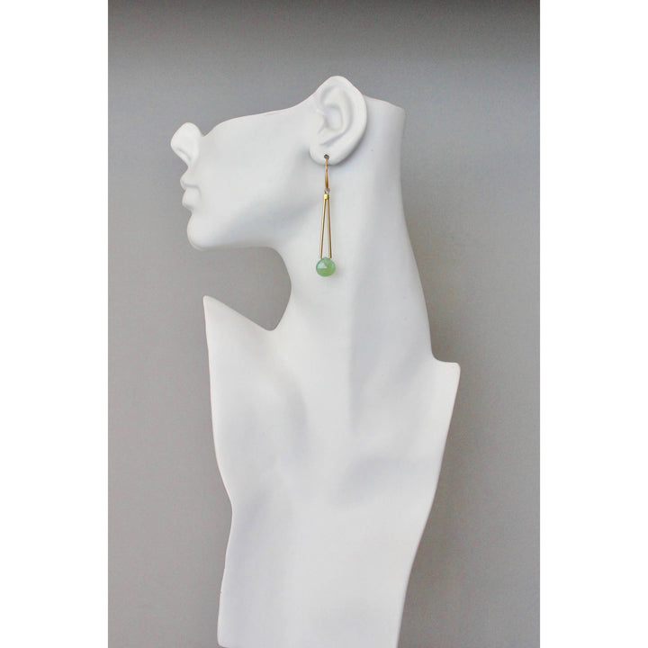 Gold dangle earring with blue-green bead on a white mannequin ear with a plain background
