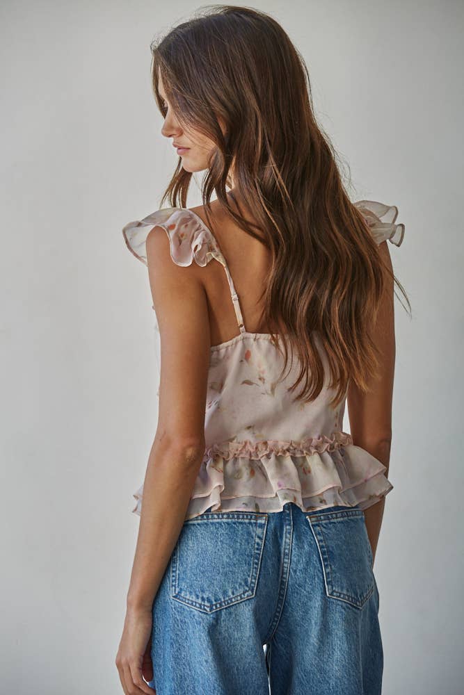 Woman wearing a pink floral blouse with ruffled sleeves and blue jeans against a plain background