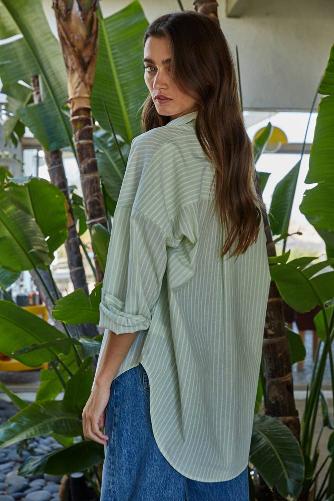 Woman wearing a light green striped shirt and blue pants standing among tropical plants.