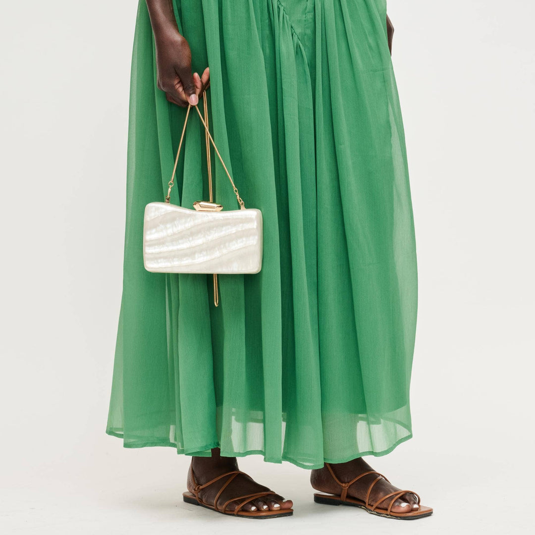 Person wearing a green dress holding a white clutch on a white background