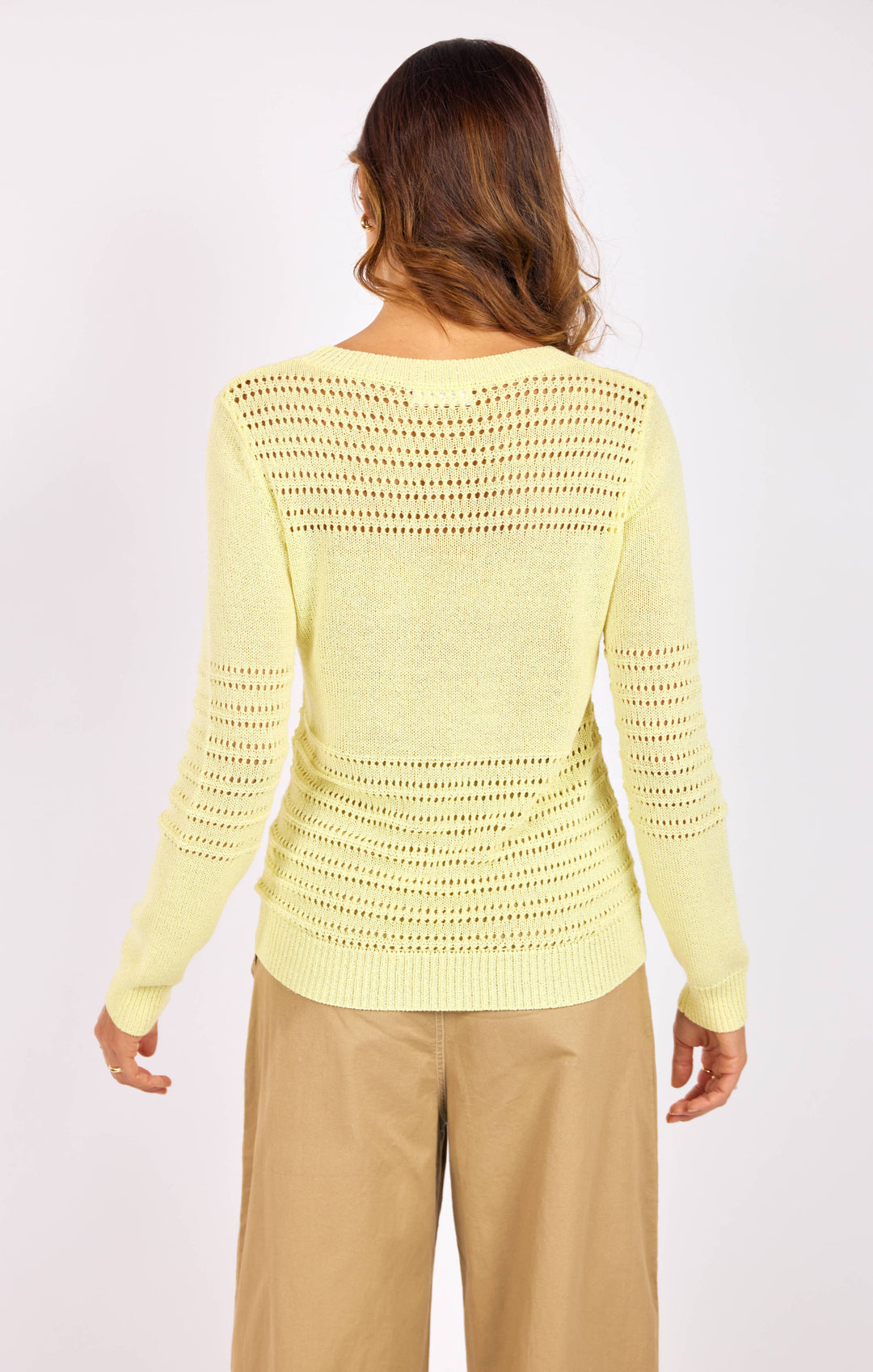 Woman wearing a light yellow crochet sweater on a white background