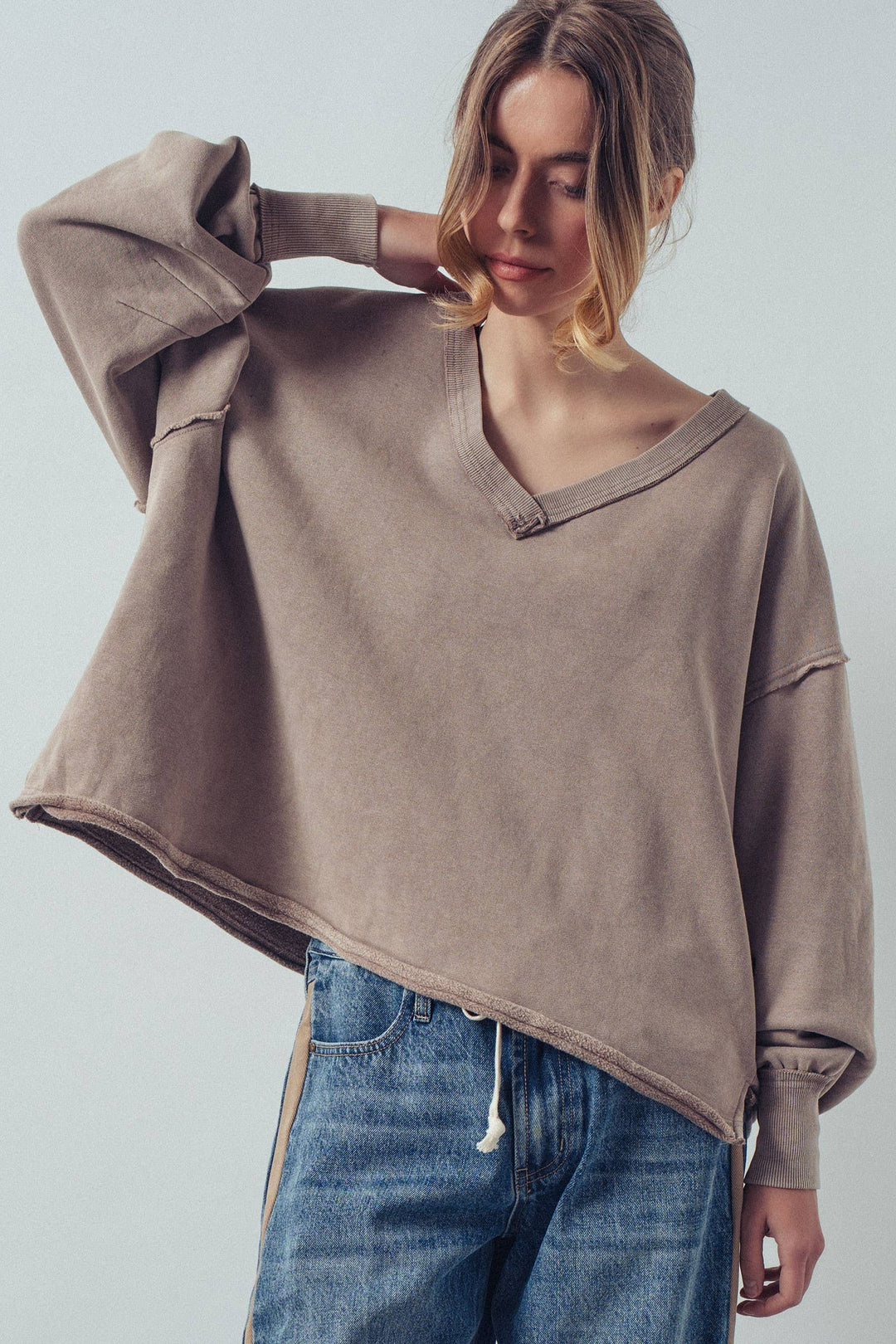 Person wearing a brown oversized sweater and blue jeans against a plain background