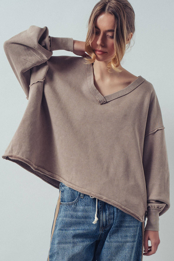 Person wearing a brown oversized sweater and blue jeans against a plain background