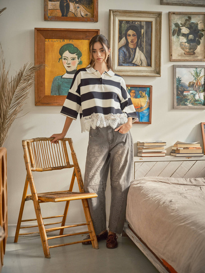 Woman in a striped knit collared shirt and gray pants standing in a room with vintage paintings on the wall.