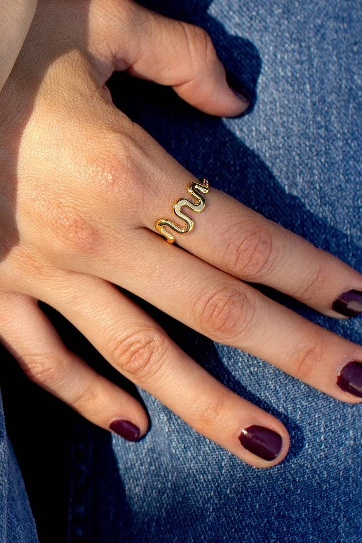 Gold snake-shaped ring on a finger with a blue denim background