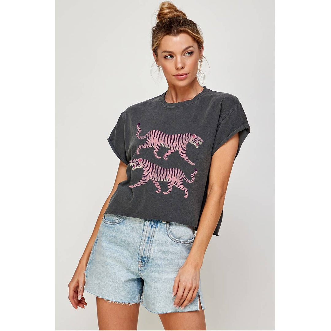 Woman wearing a dark gray cropped t-shirt with pink tiger design and light blue denim shorts on a plain background