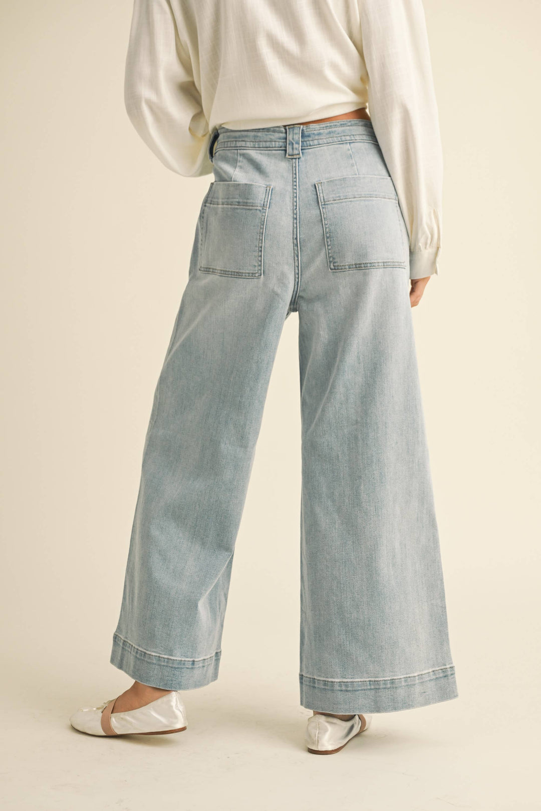 Light wash denim wide leg cropped pants worn by a woman on a beige background